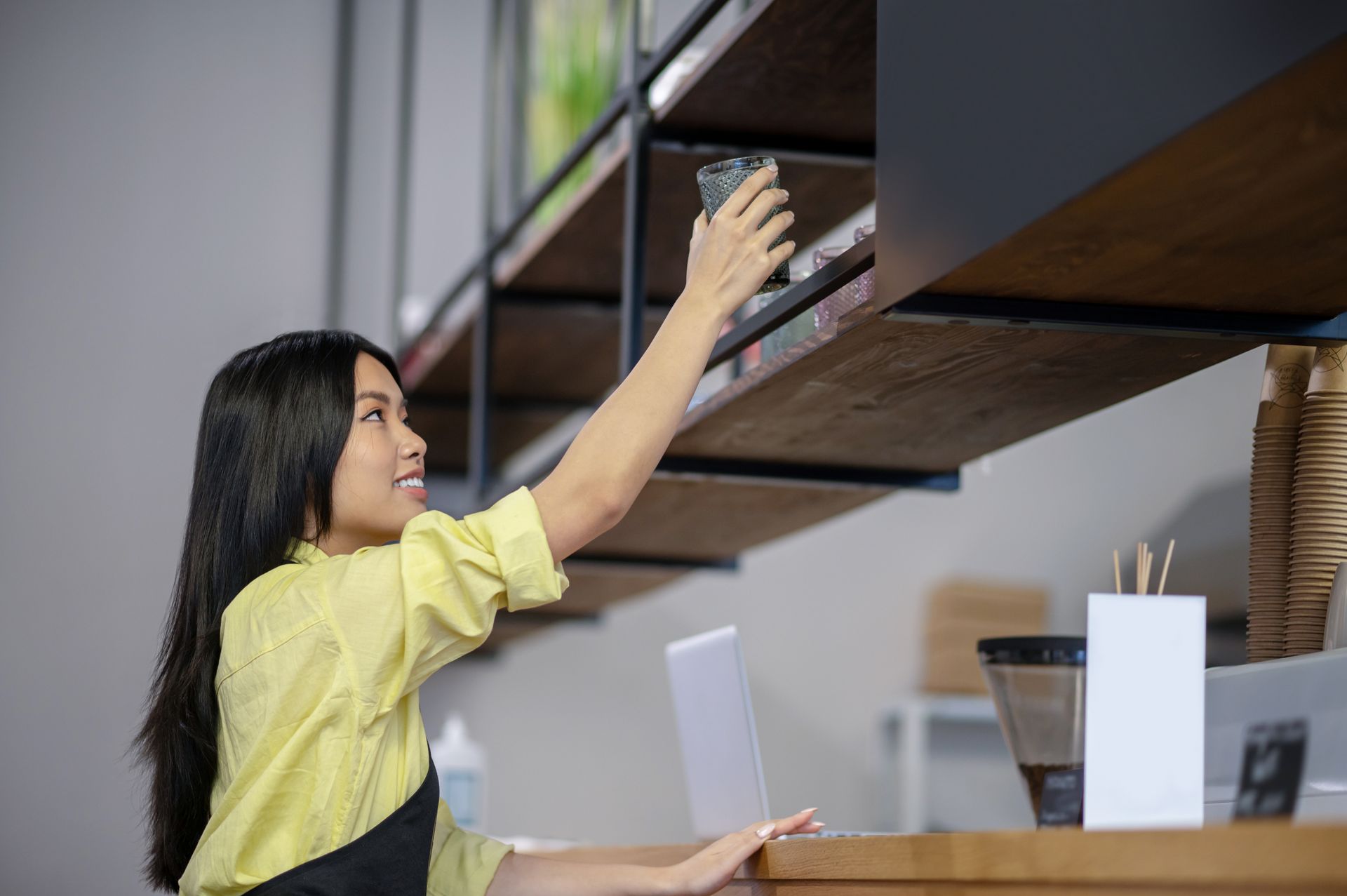 A woman is reaching for something on a shelf in a kitchen.