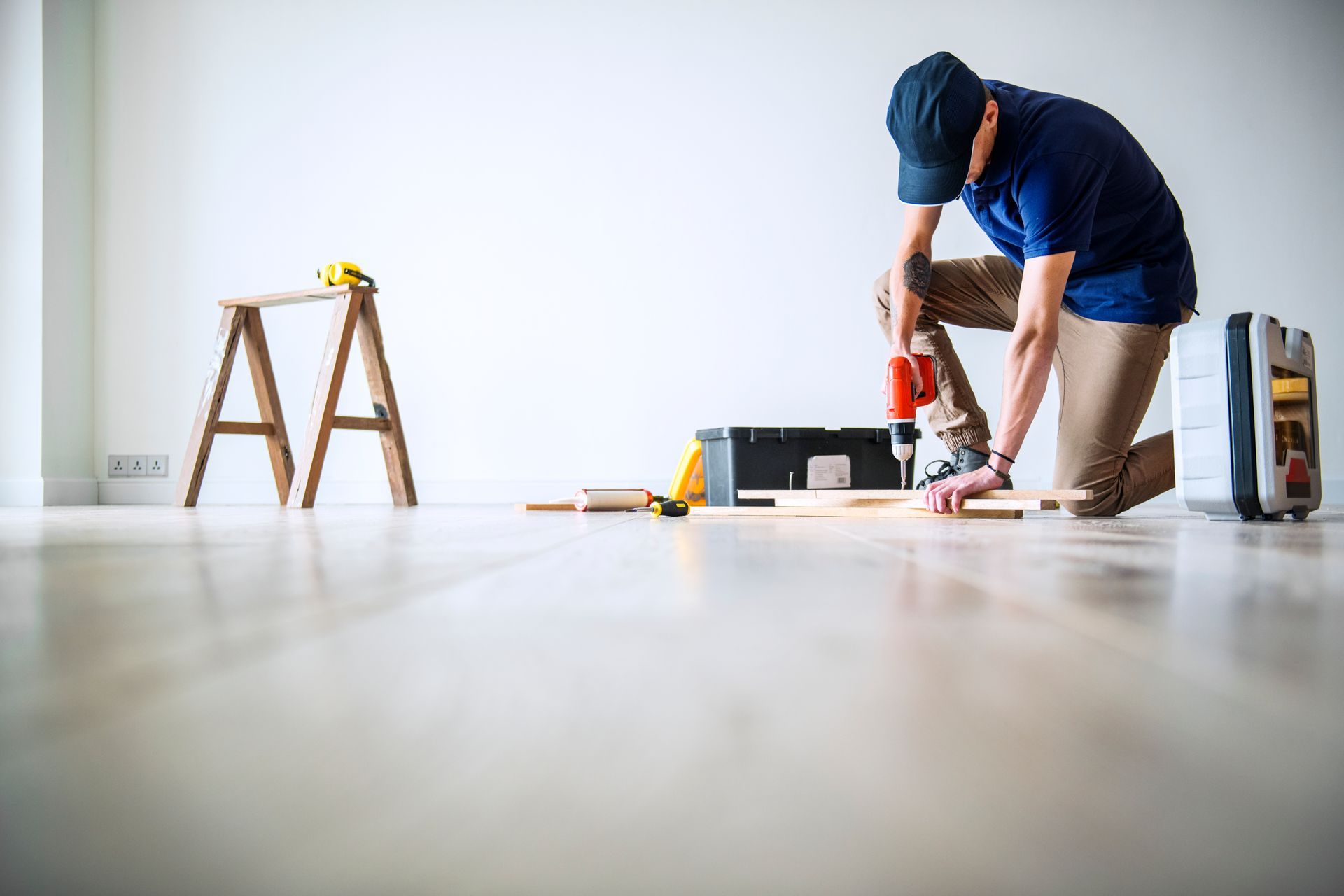 A man is kneeling on the floor working on a piece of wood.