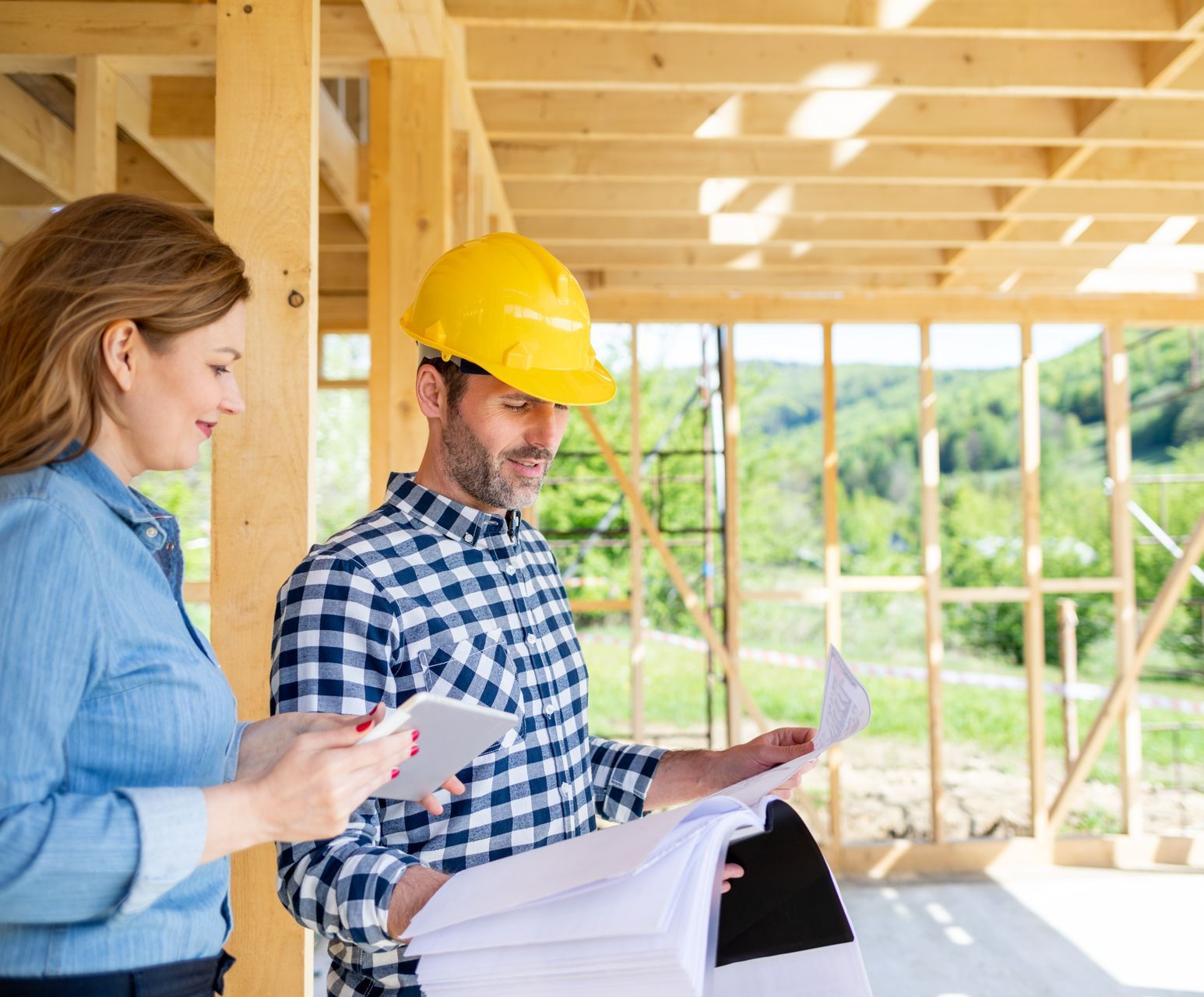 A man and a woman are looking at a blueprint on a construction site.