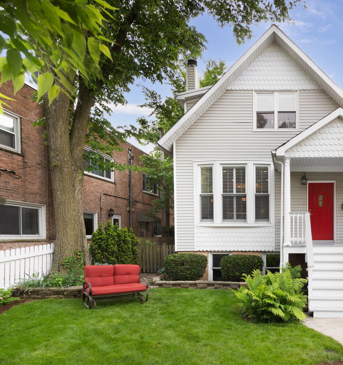 A white house with a red door and a red bench in front of it.