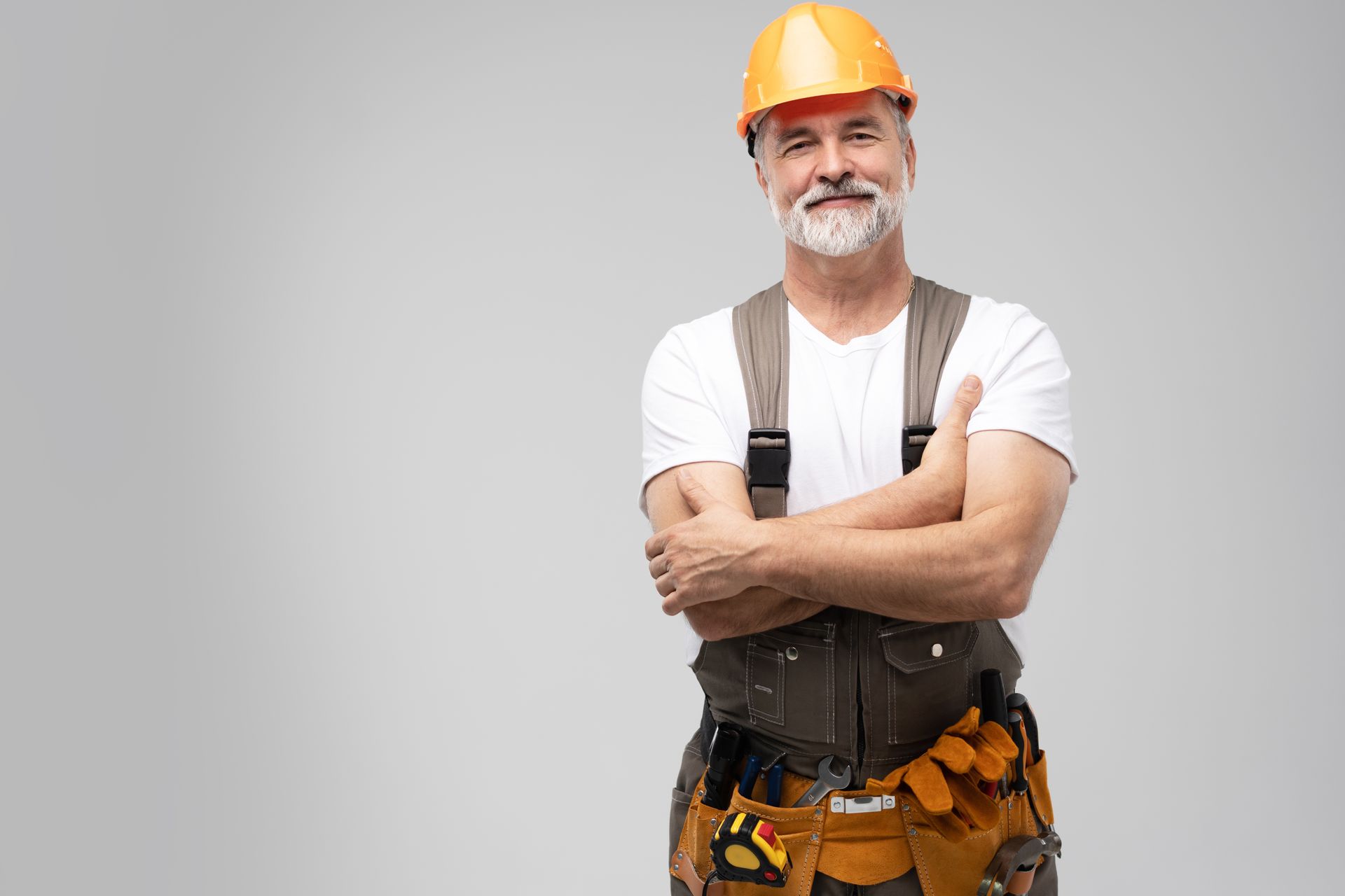 A man wearing a hard hat and overalls is standing with his arms crossed.