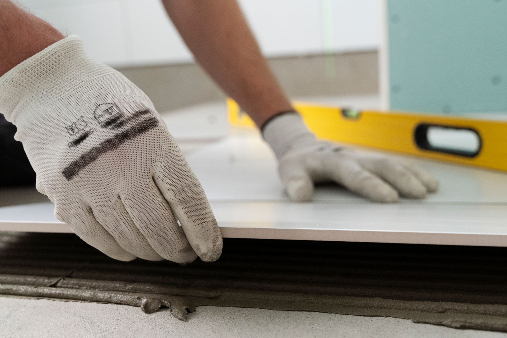A person wearing gloves is laying a tile on the floor.