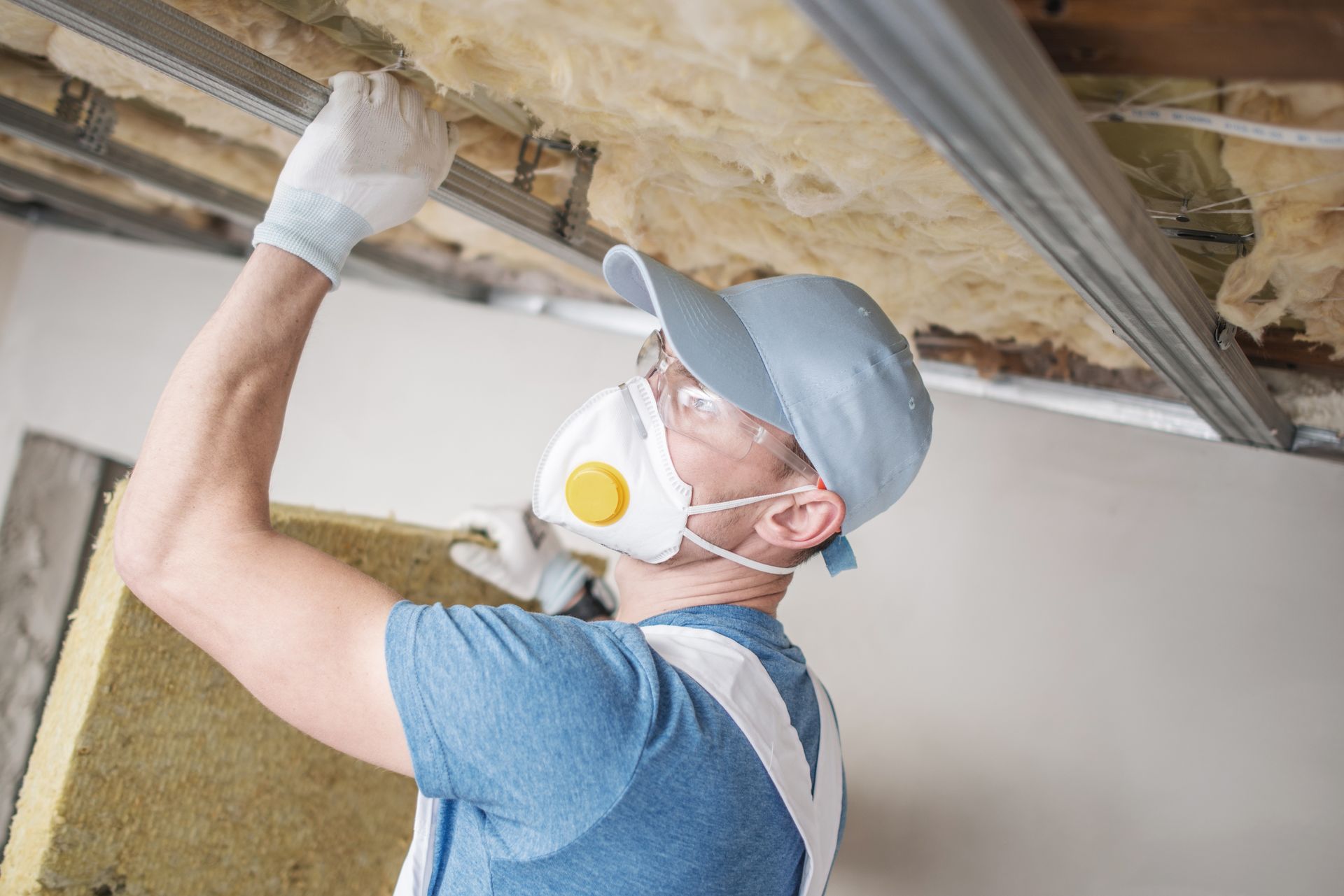 A man wearing a mask and gloves is insulating the ceiling.