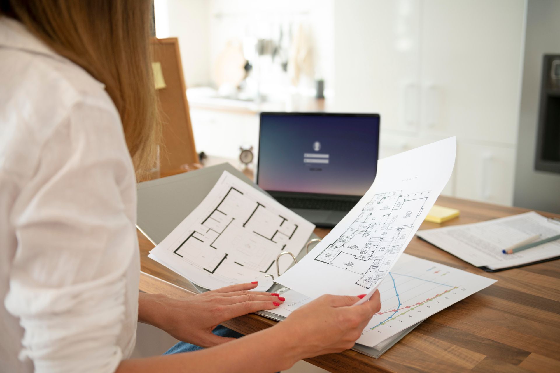 A woman is holding a piece of paper in front of a laptop computer.