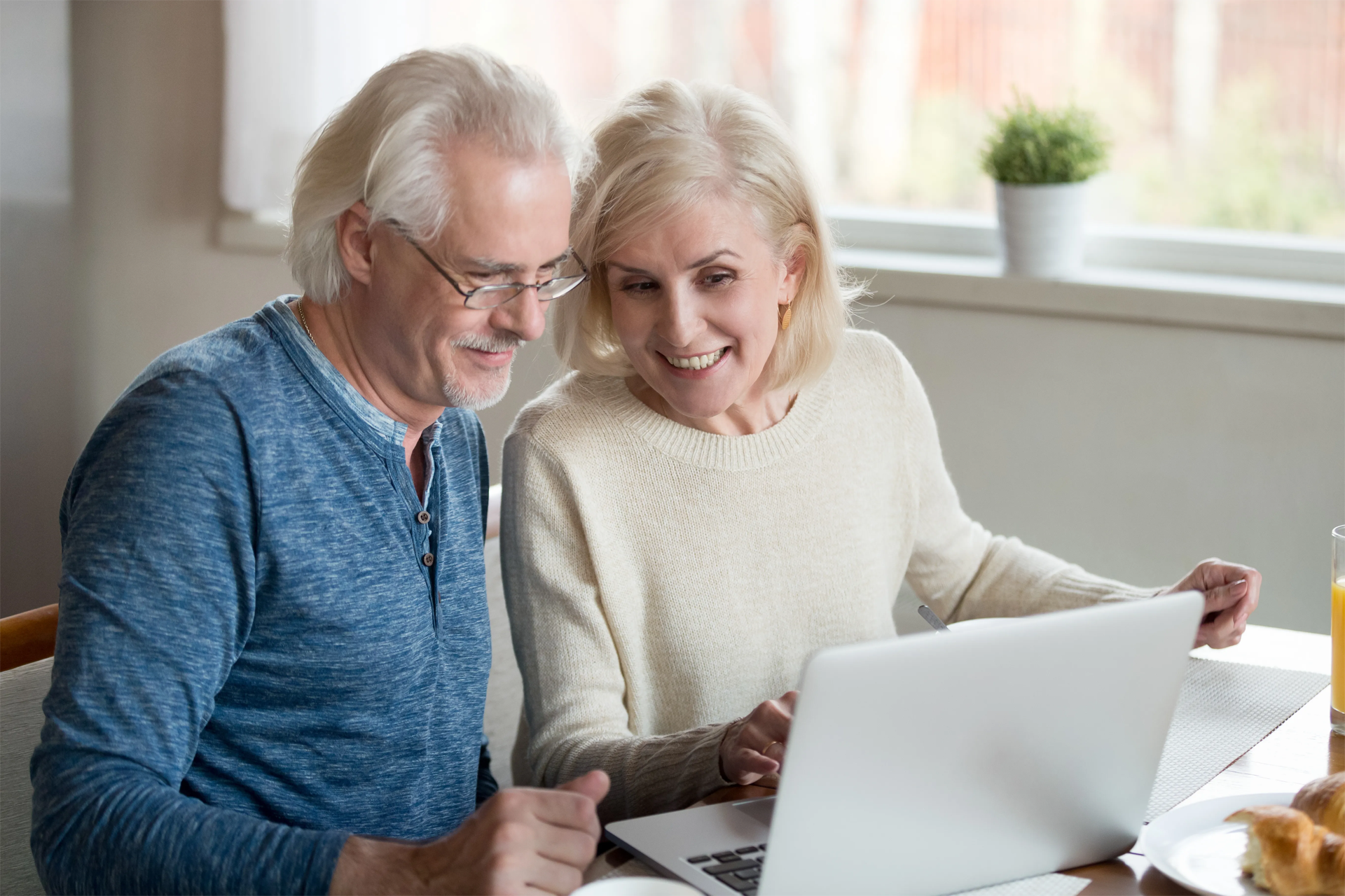 A man and a woman are sitting on a couch looking at a laptop computer.
