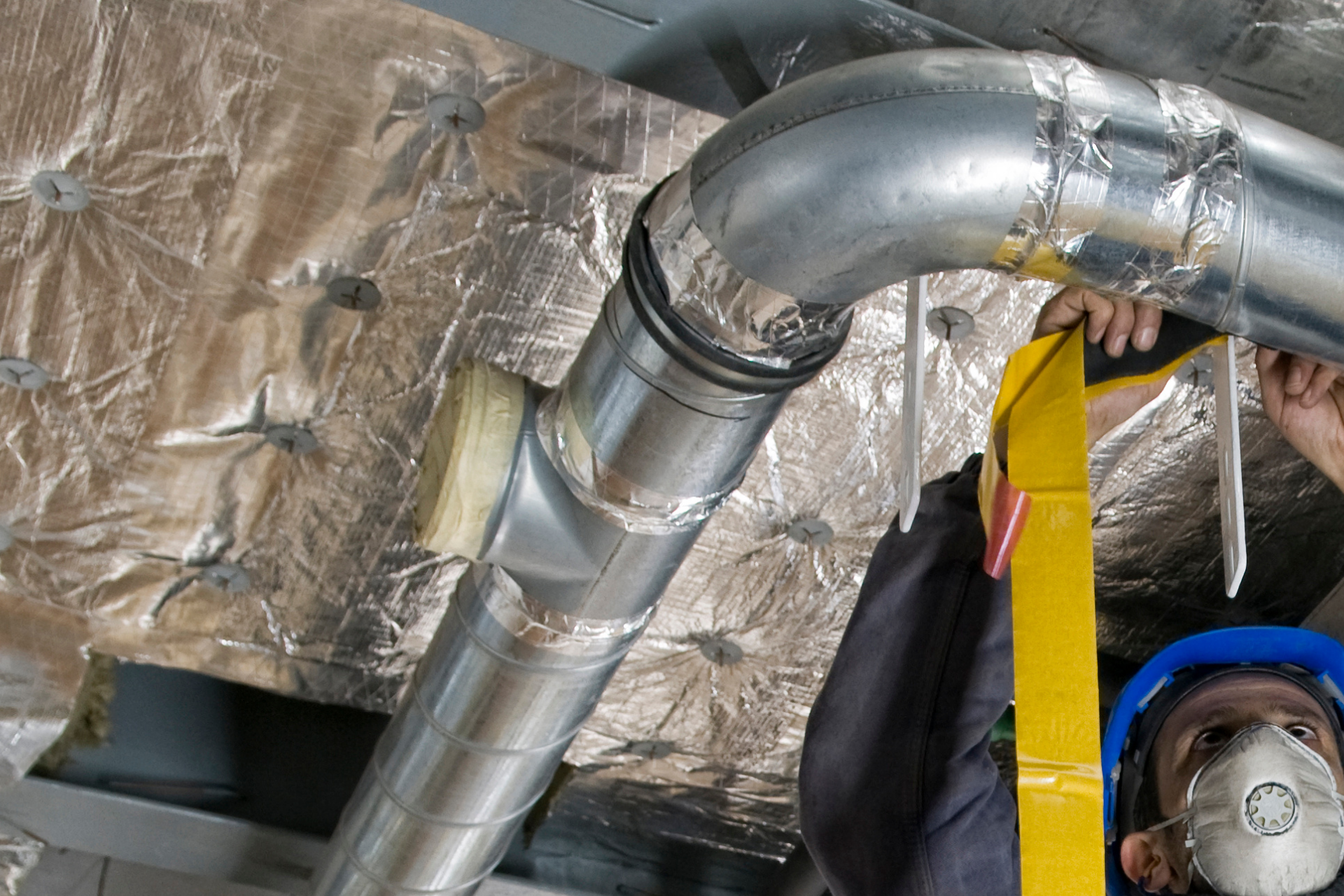 A man wearing a mask is working on a metal pipe.