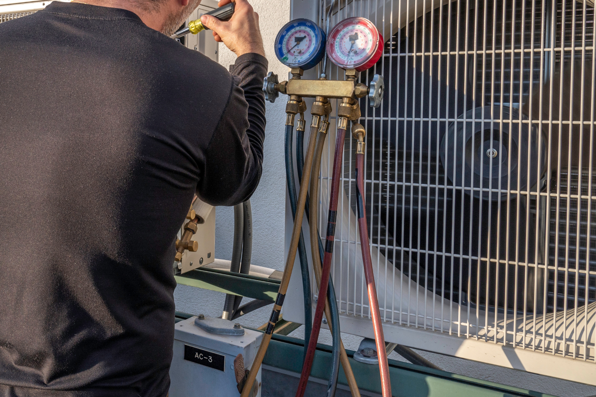 A man is working on an air conditioner outside of a building.