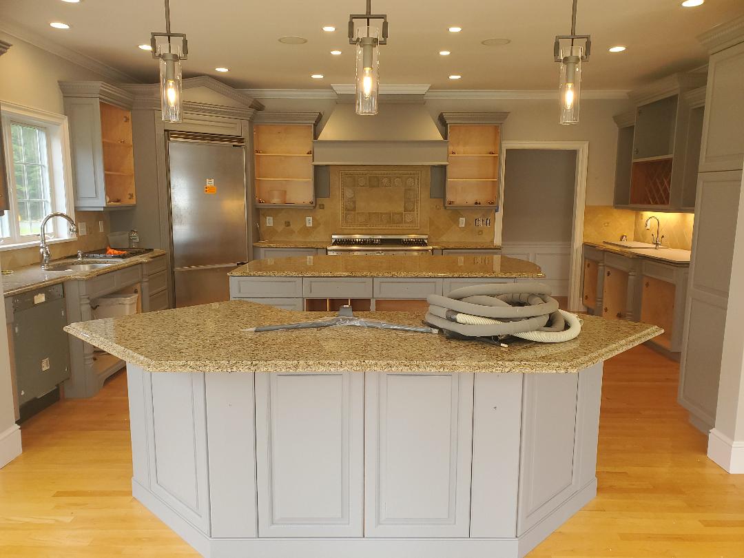 A kitchen undergoing renovation with gray cabinets, granite countertops, and pendant lights.