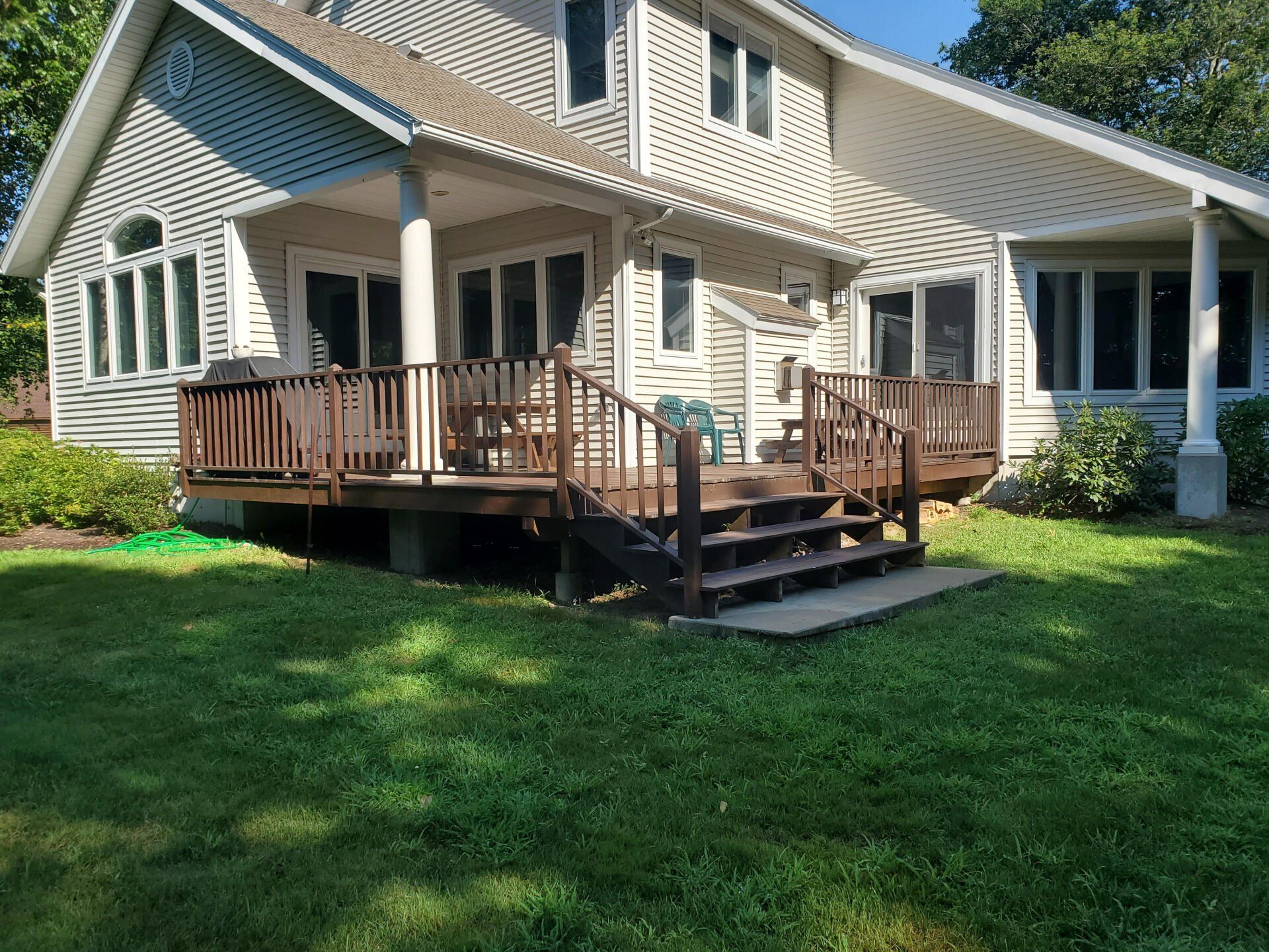 Backyard deck with stairs, brown railing, extending from a two-story beige house, green lawn.