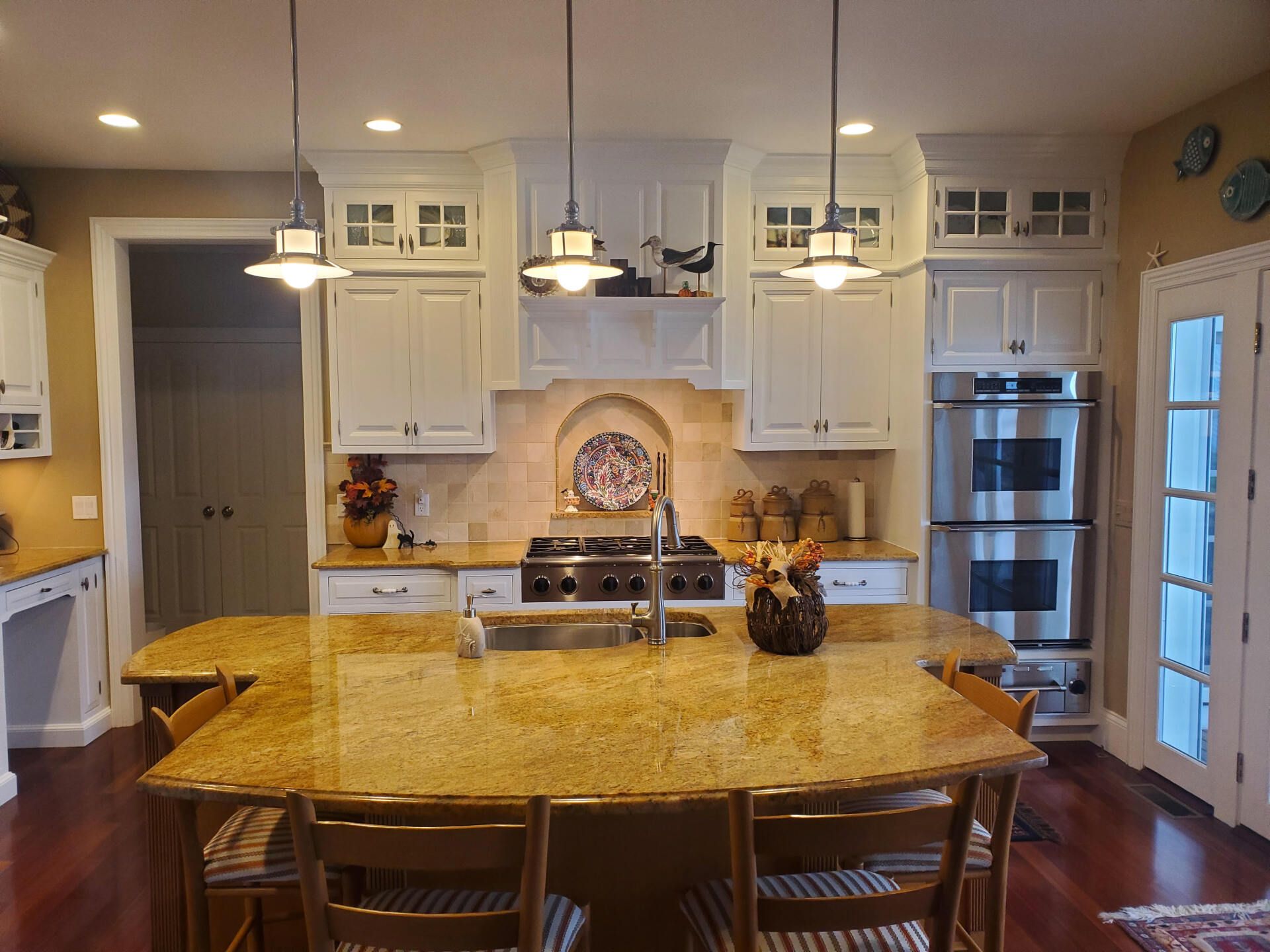 Spacious kitchen with white cabinets, granite island, stainless steel appliances, and hanging lights.