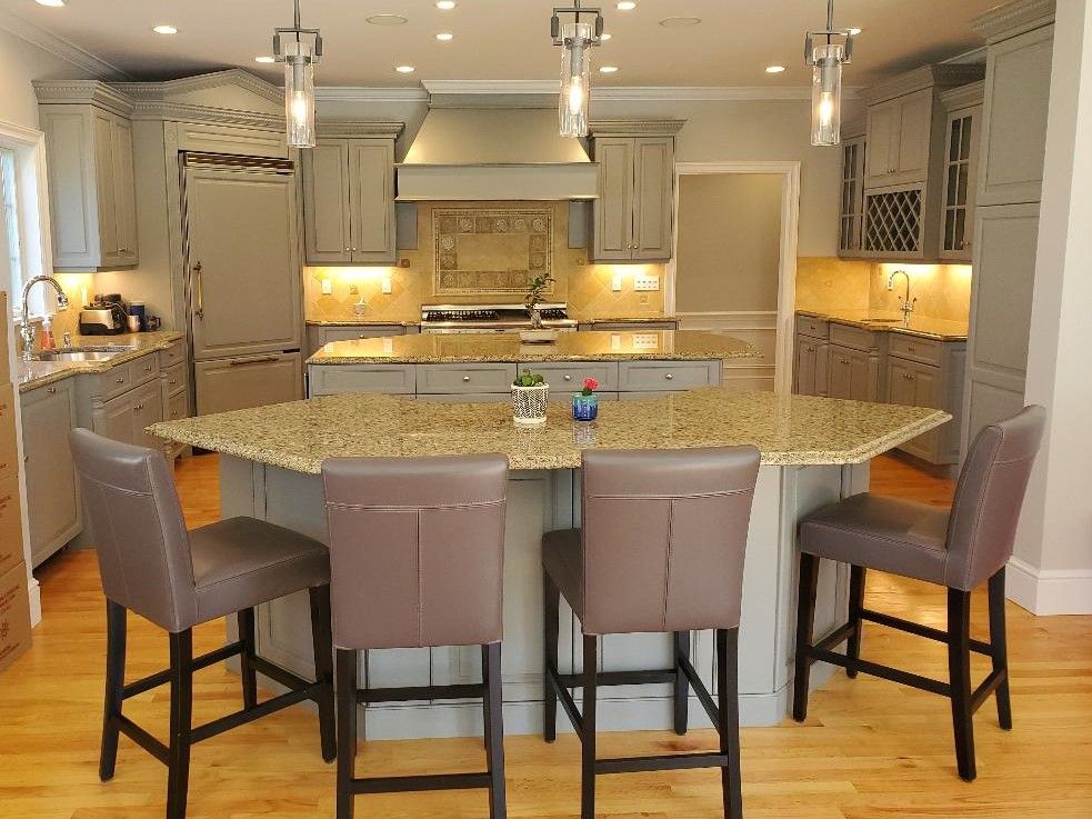 A modern gray kitchen with a granite island, gray cabinets, and four brown leather bar stools.