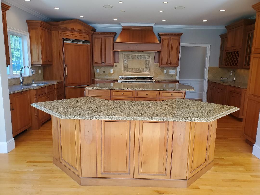 A spacious kitchen with light wood cabinets, granite countertops, and a large island.