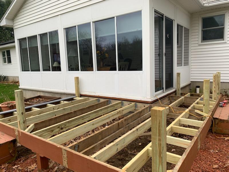 Partially constructed deck attached to a white house with large windows; wood framing and support posts visible.