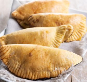 Cuatro pasteles horneados de color marrón dorado con bordes ondulados sobre una bandeja blanca con un paño de color neutro.