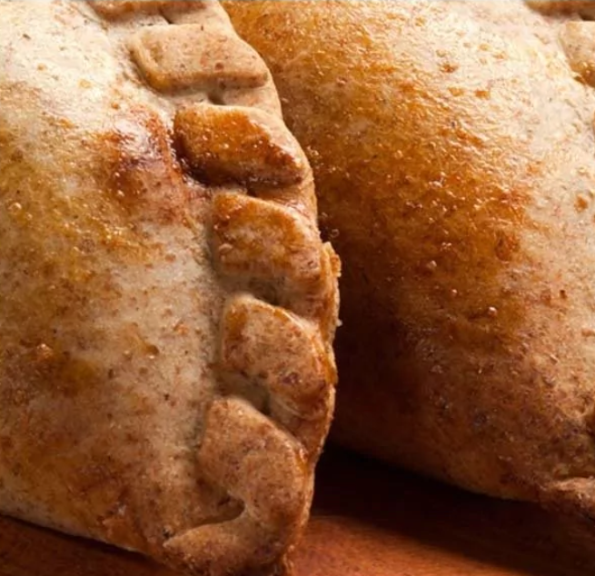 Dos empanadas horneadas, de color dorado y con bordes ondulados, primer plano.
