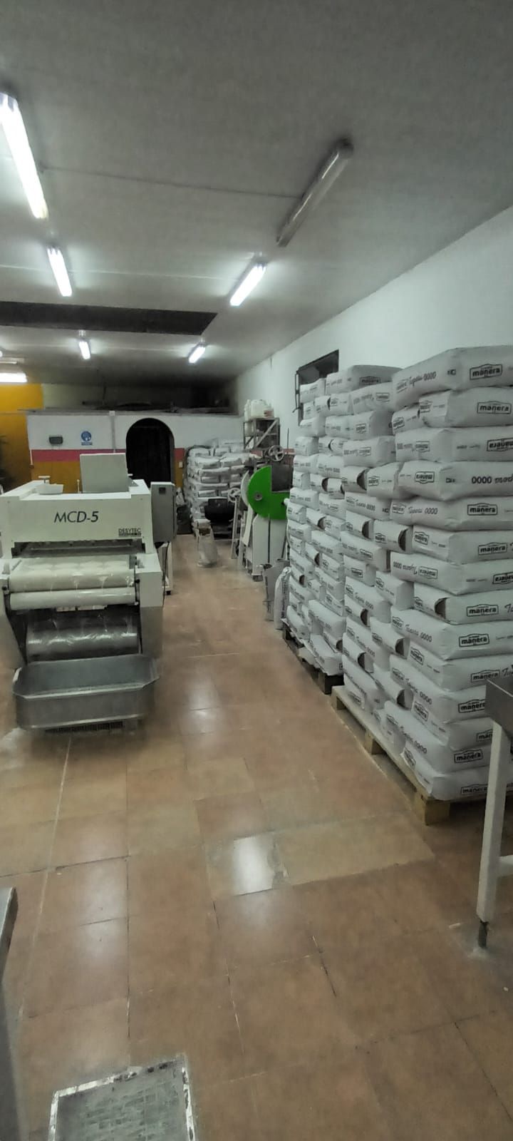 Dentro de una cocina comercial con equipo para procesar masa, los sacos de harina se apilan en el lado derecho.