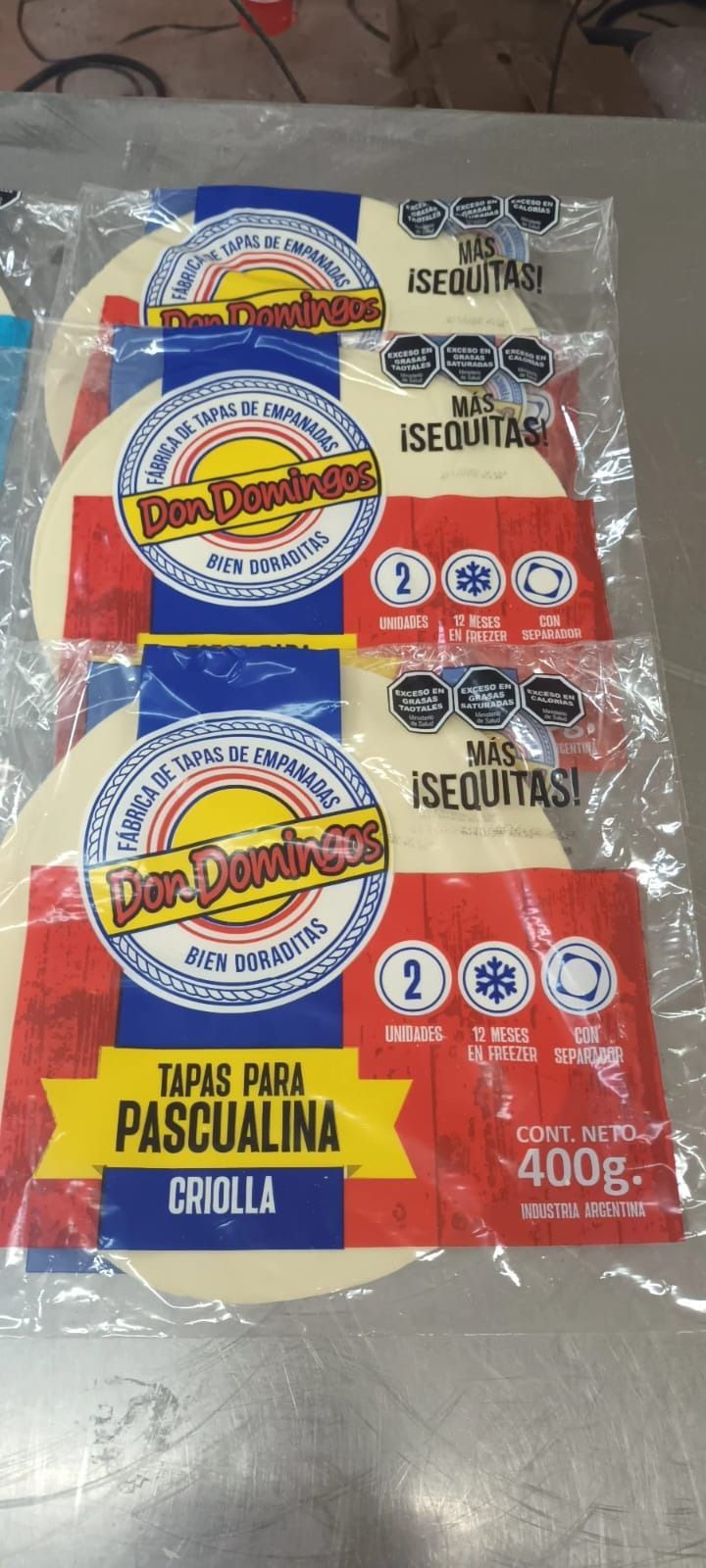 Tres paquetes de tortillas envueltos en plástico. Los paquetes tienen etiquetas rojas, azules y amarillas con un logotipo.