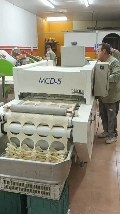 Persona operando una máquina MCD-5 blanca cortando masa. Los círculos de masa cortados caen en un recipiente.