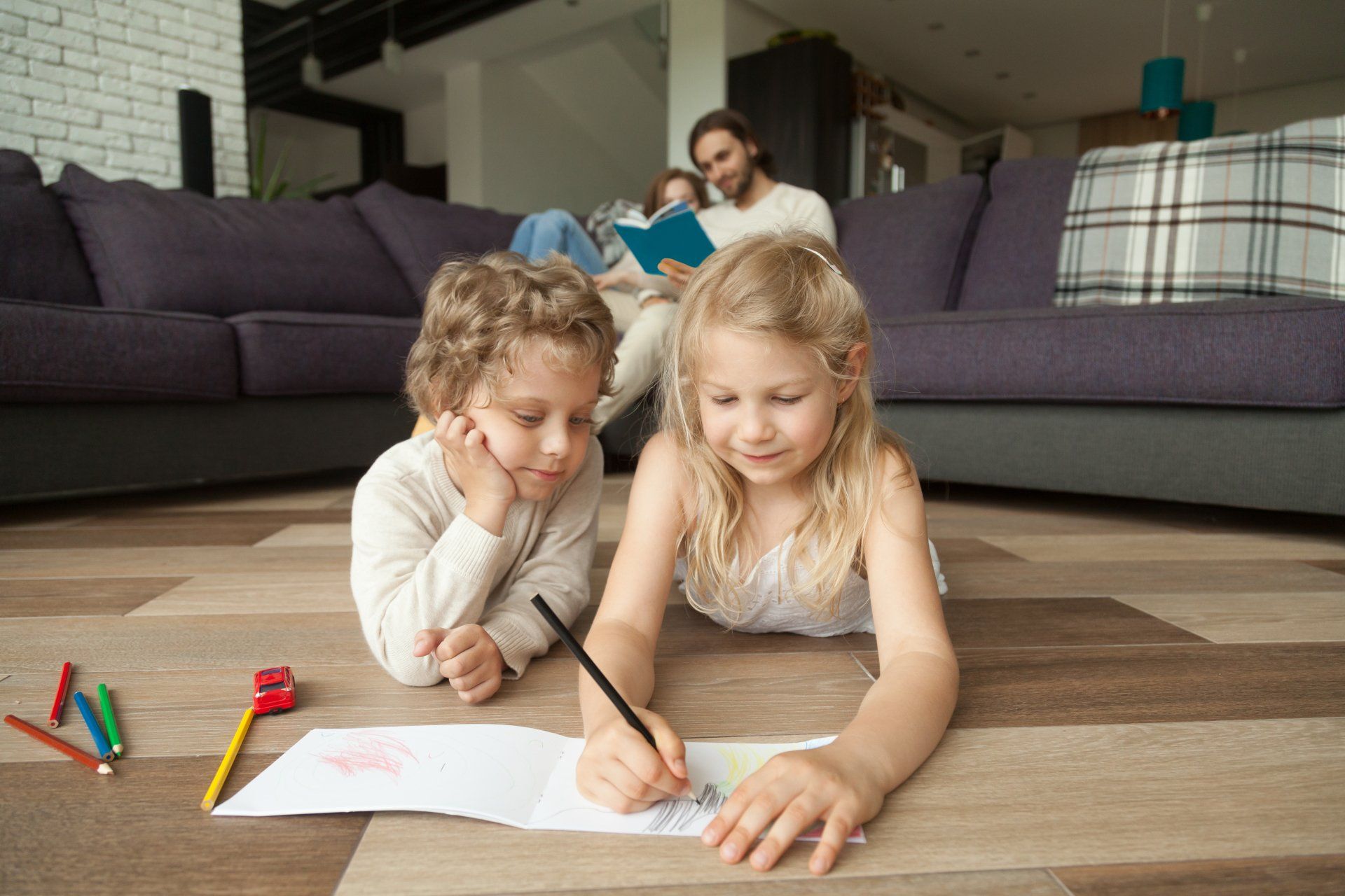A boy and a girl are laying on the floor drawing.