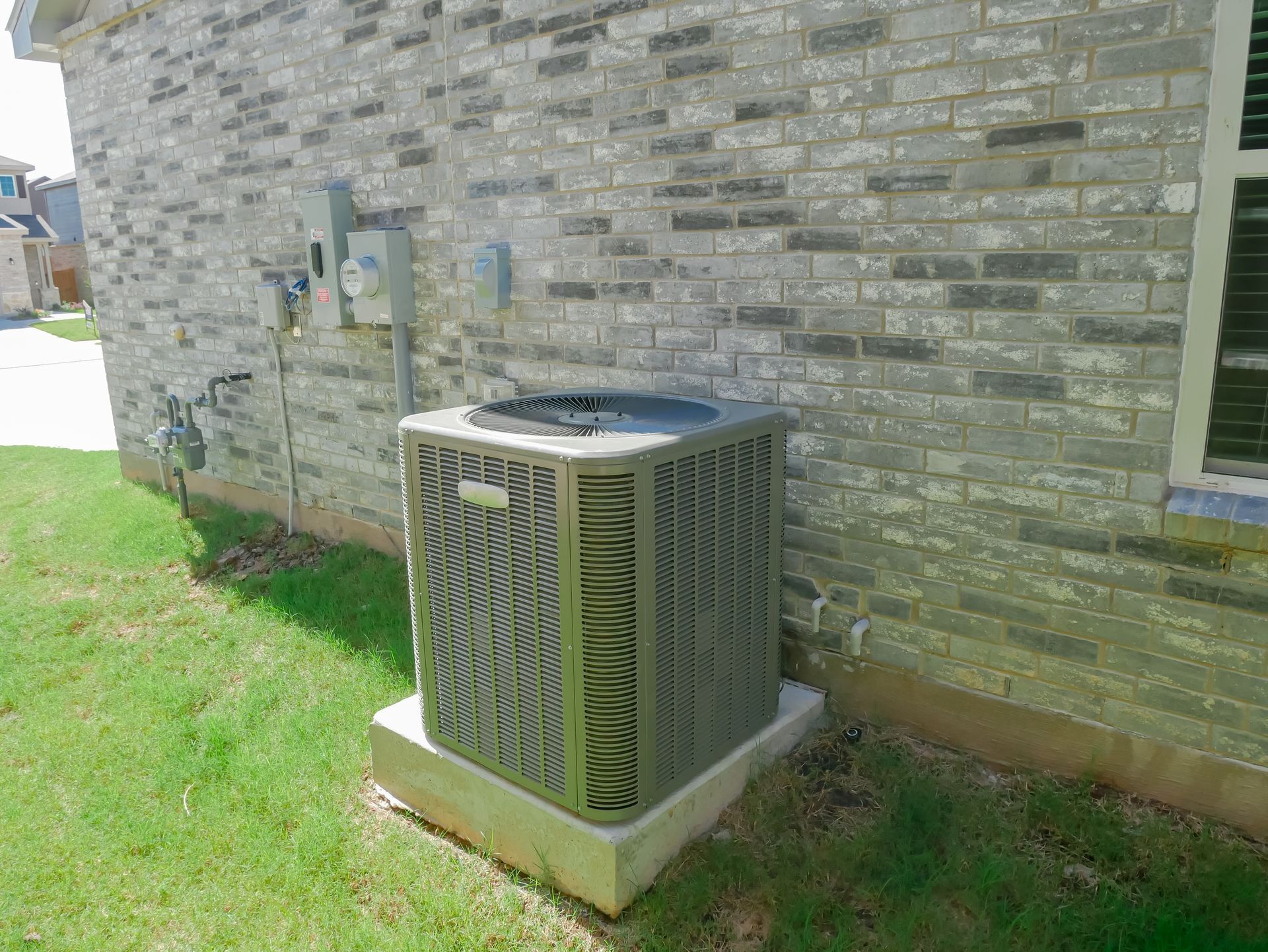 Outdoor air conditioning unit beside a stone house wall on a grassy lawn