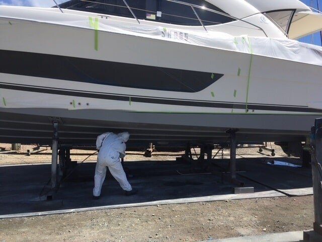 A Man In A White Suit Is Spray Painting The Bottom Of A Boat — Edge's Boatyard In Jubilee Pocket, QLD