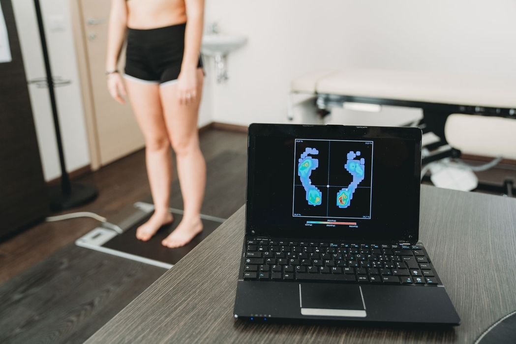 Donna in piedi su una pedana di pressione mentre un computer portatile visualizza l'analisi della pressione del piede in uno studio medico.