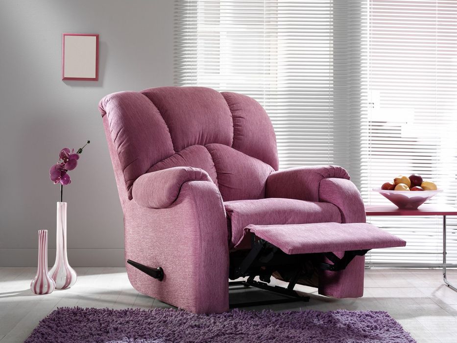 Poltrona reclinabile rosa con poggiapiedi esteso, su un tappeto viola, vicino a un tavolo e a una finestra.