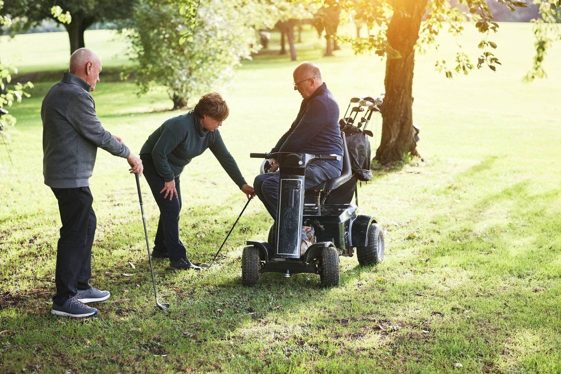 Tre golfisti su un campo da golf soleggiato: uno su sedia a rotelle, gli altri due aiutano con le mazze da golf.