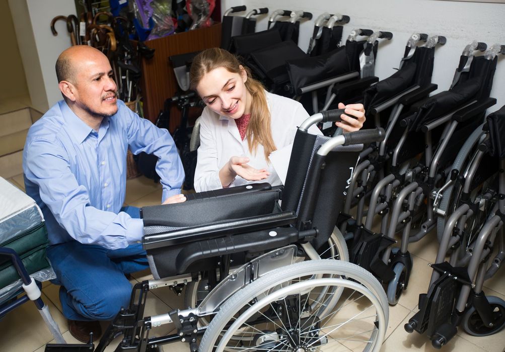 Un uomo e una donna esaminano una sedia a rotelle in un negozio di forniture mediche. La donna indica mentre l'uomo la osserva.