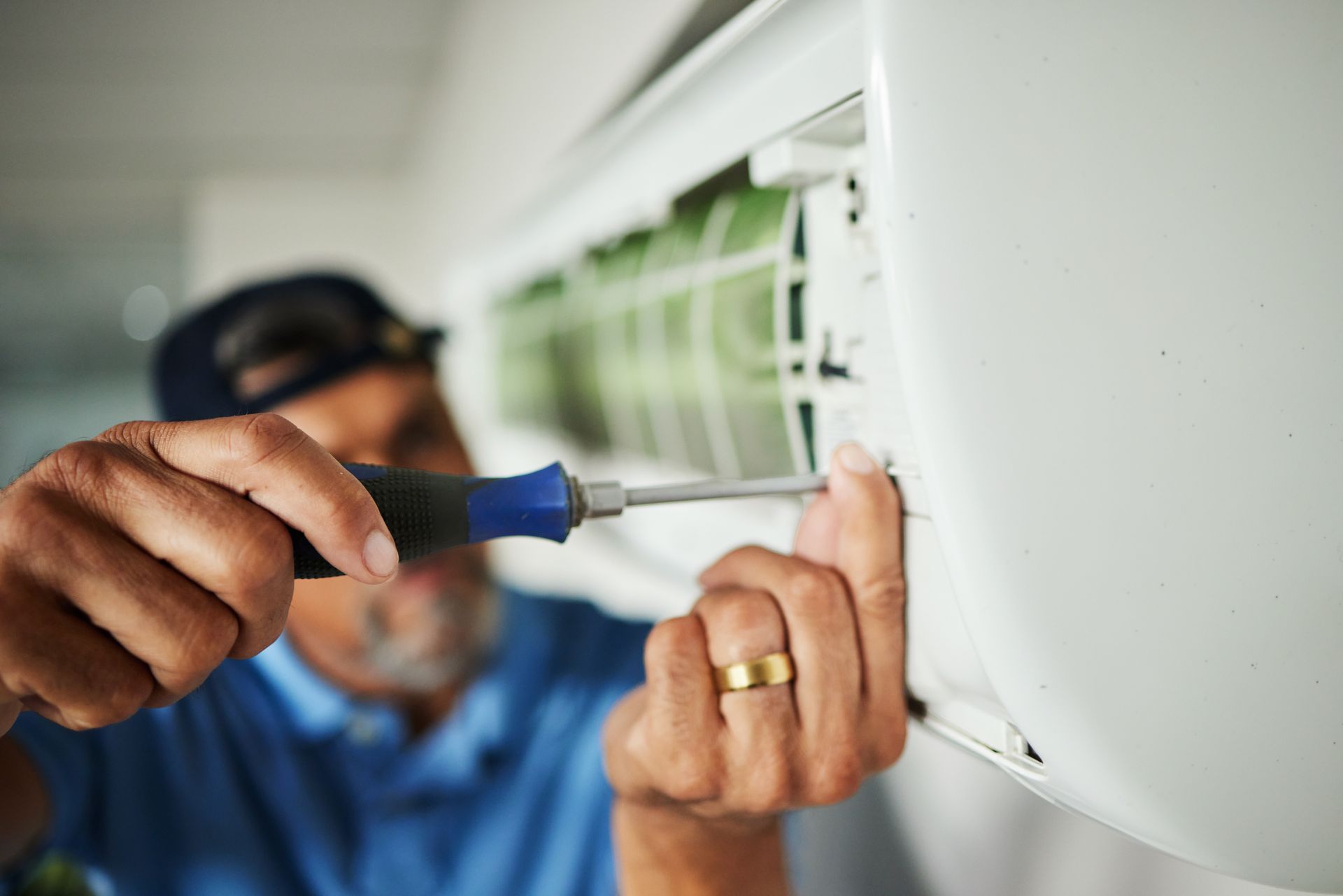 Technician in a blue shirt uses a screwdriver to repair a wall-mounted air conditioning unit. Technician in a blue shirt uses a screwdriver to repair a wall-mounted air conditioning unit.