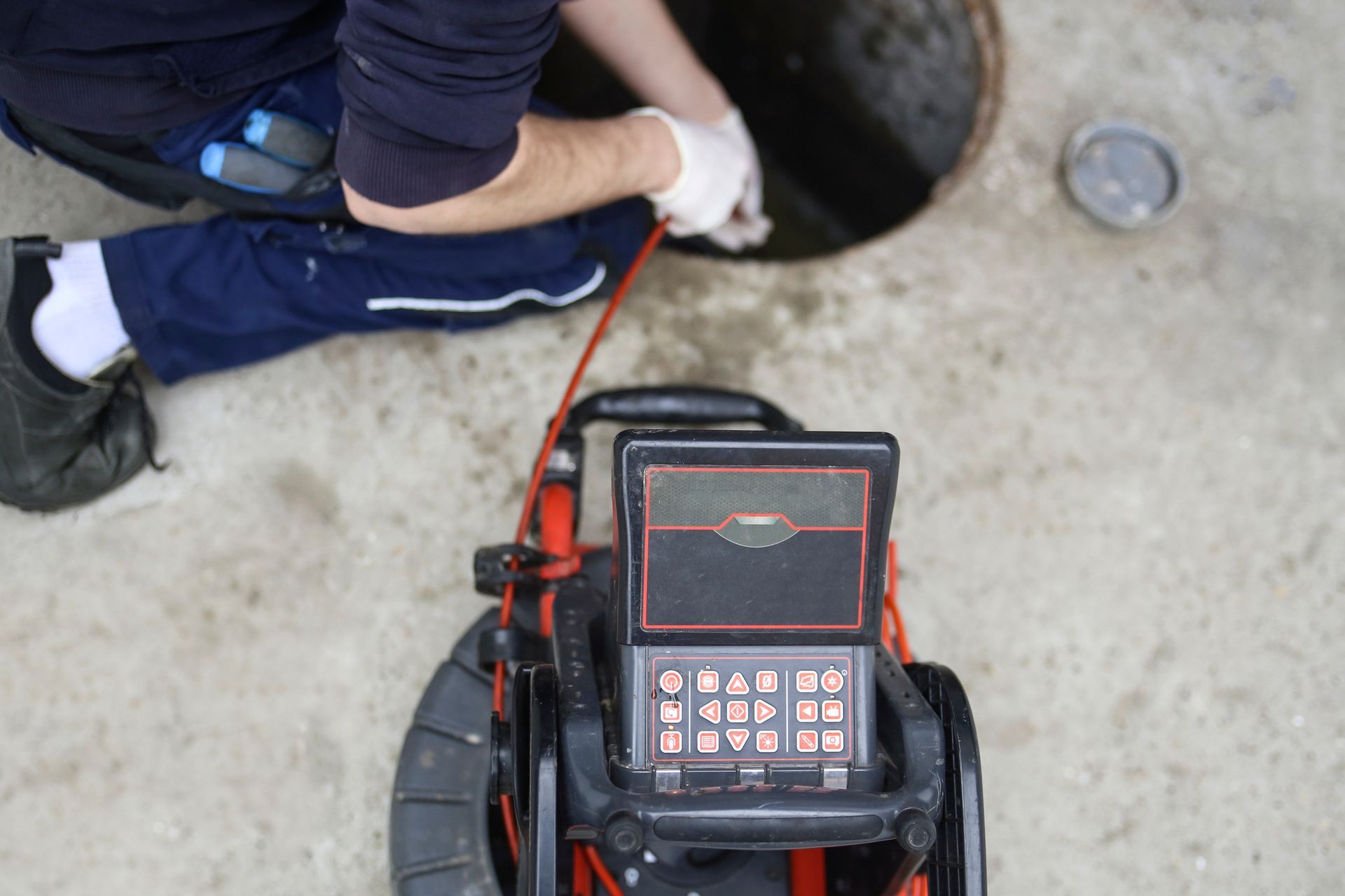 Worker uses sewer camera to inspect inside a manhole.