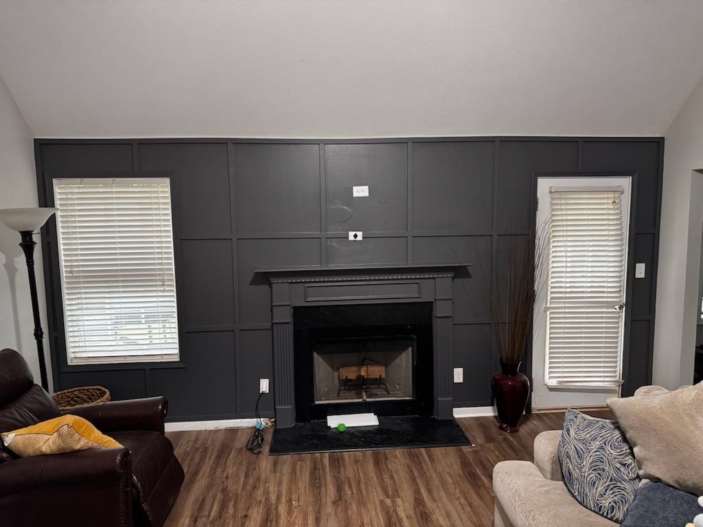 Dark gray paneled accent wall with fireplace, two windows with blinds, and hardwood floors.