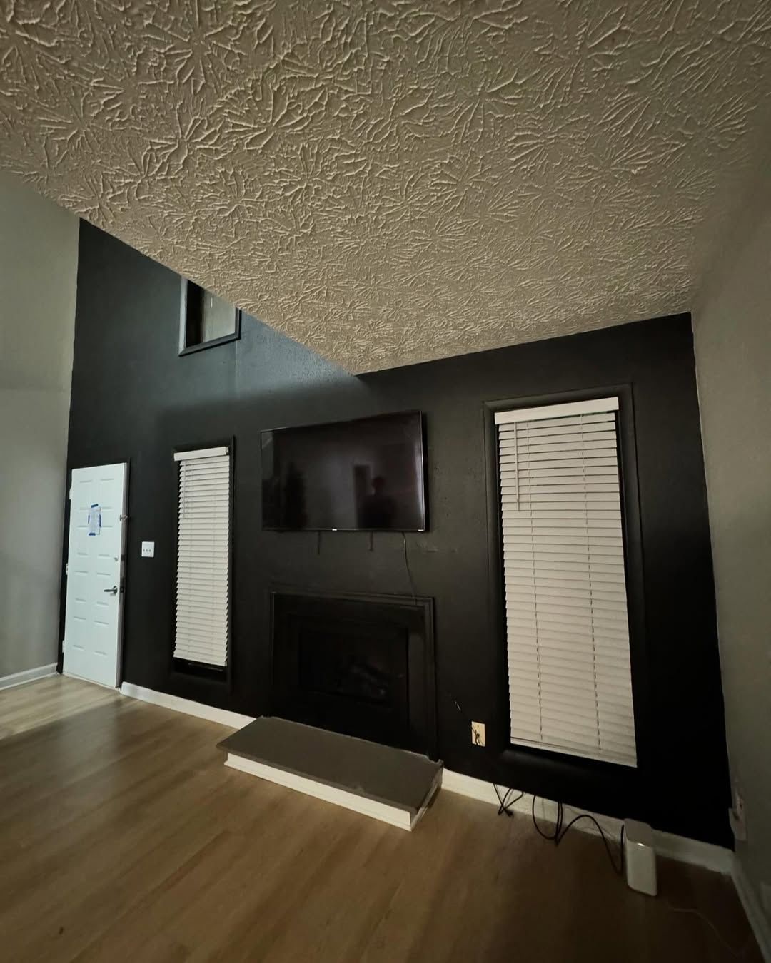 Living room with black accent wall, TV, fireplace, and blinds.