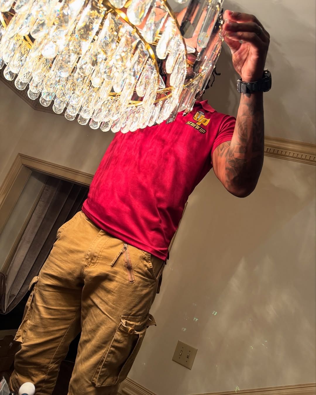 Man in red shirt and tan pants working on a crystal chandelier.