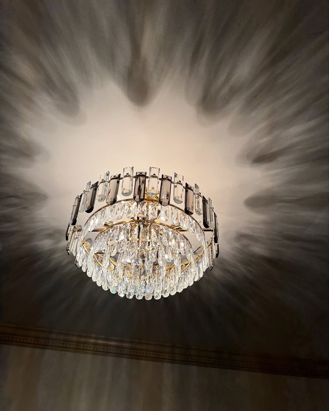 Crystal chandelier casting star-like shadows on a ceiling.