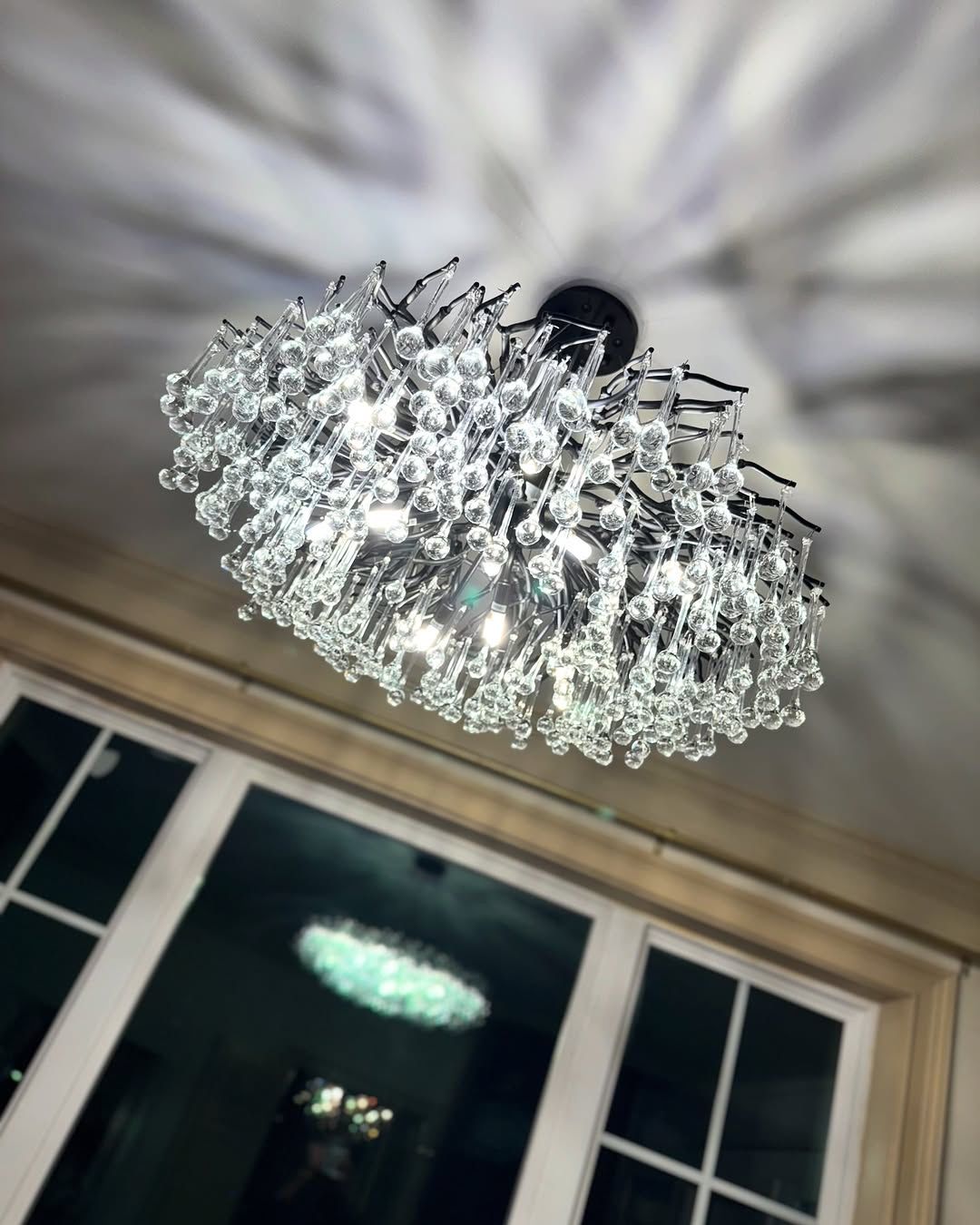 Crystal chandelier mounted on a white ceiling, casting light patterns.