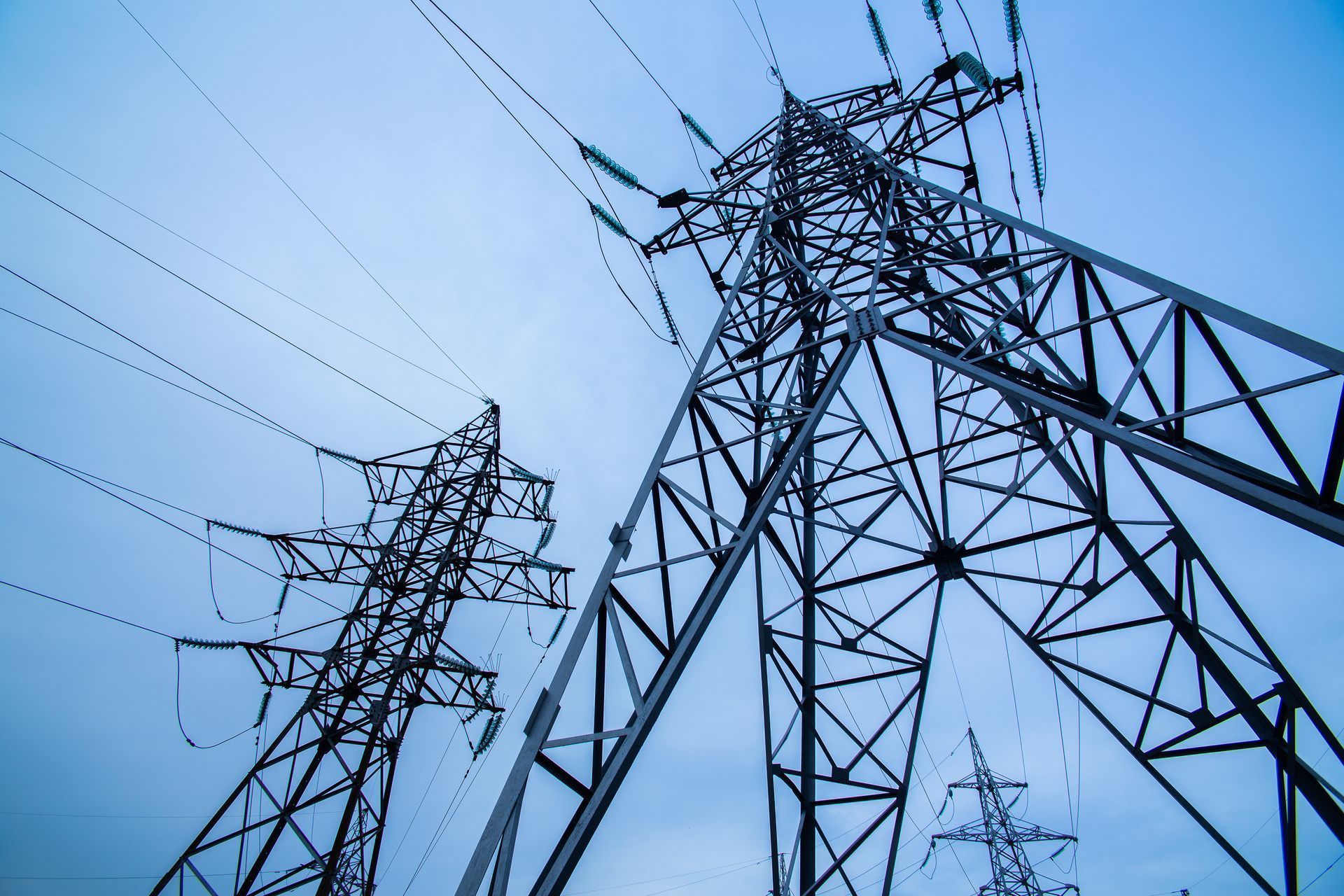 Overhead power lines and metal towers against a blue sky.