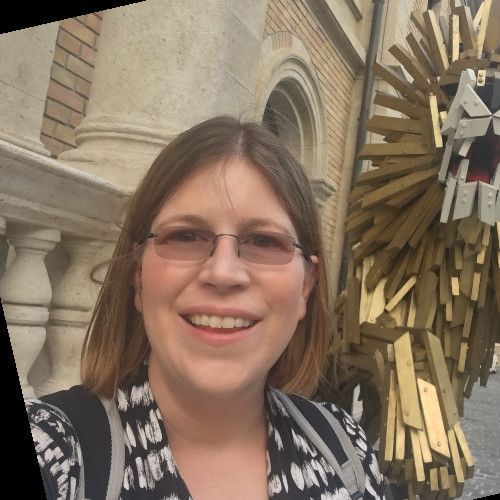 Man in a blue blazer and striped shirt, smiling, indoors with plants and light wood floors.