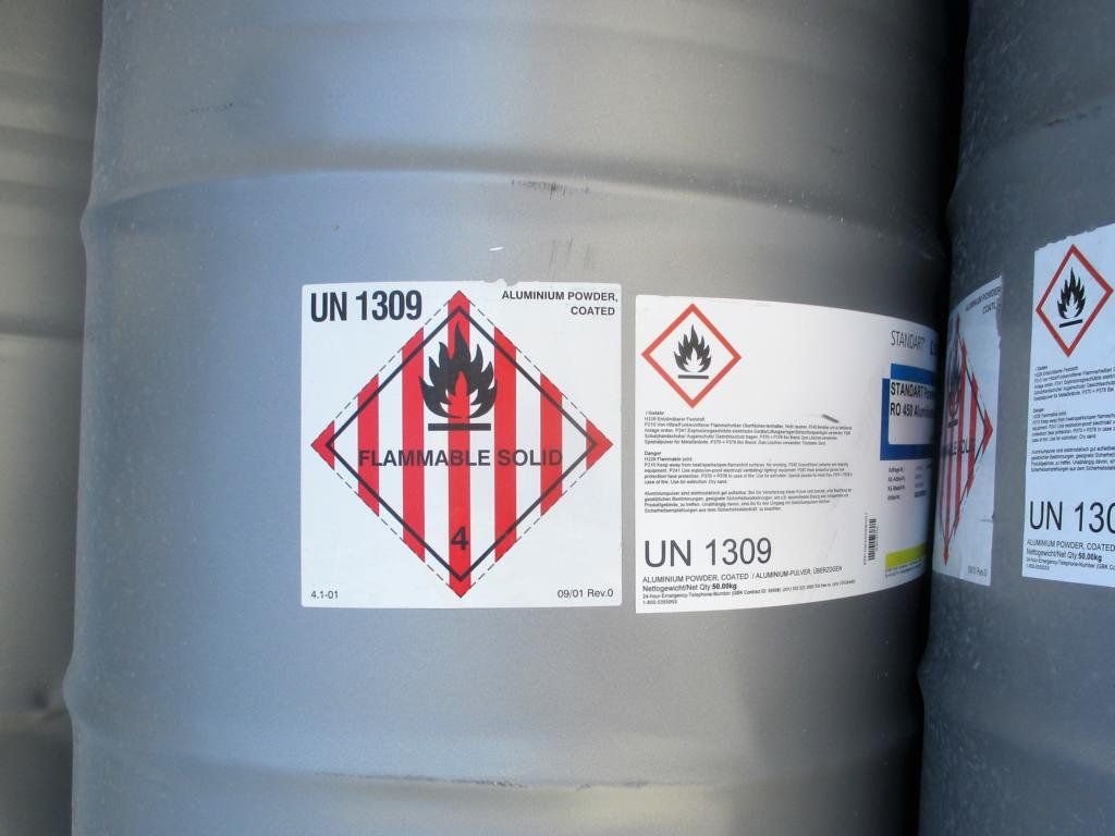 Graues Fass mit Etikett „Entzündbarer Feststoff“, rautenförmigem Symbol mit Feuer und UN 1309.