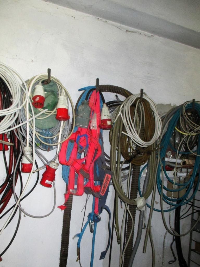 Aufgerollte Stromkabel hängen an Haken an einer weißen Wand; rote und weiße Stecker sind zu sehen.