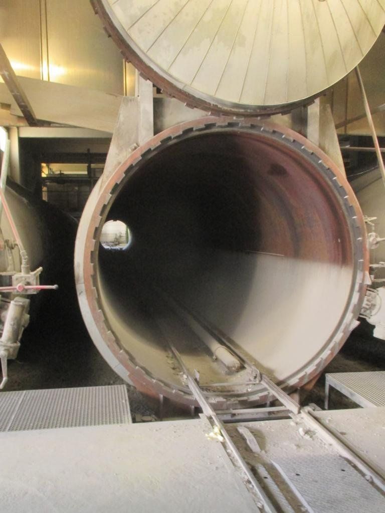 Offener industrieller Autoklav, zylindrisch mit innenliegenden Schienen, offene Tür, zementfarben.