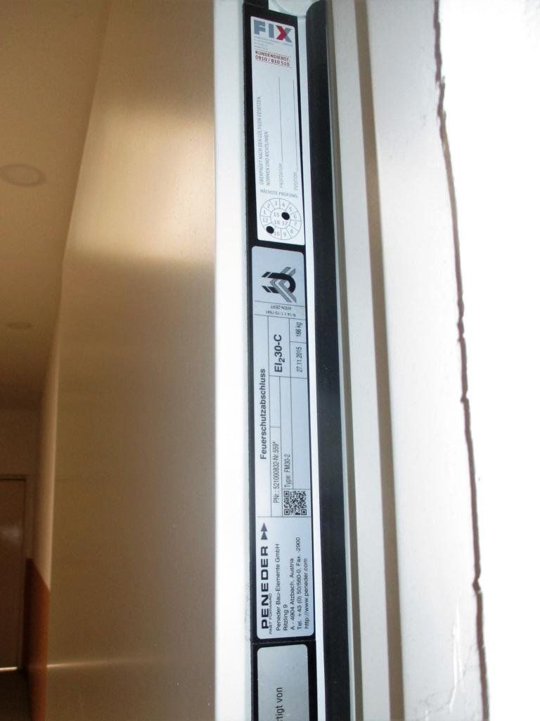 Ein Brandschutzschild an einem weißen Türrahmen in einem Gebäudeflur.