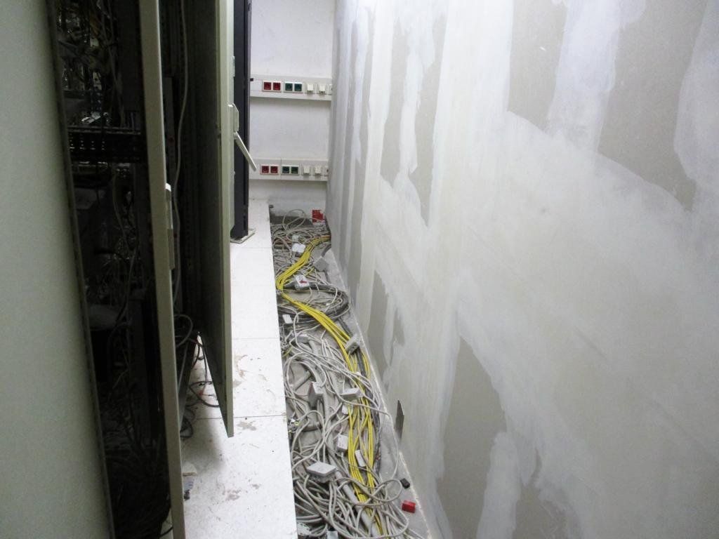 Schmaler Raum mit unverputzten Trockenbauwänden und freiliegenden elektrischen Leitungen auf dem Boden.