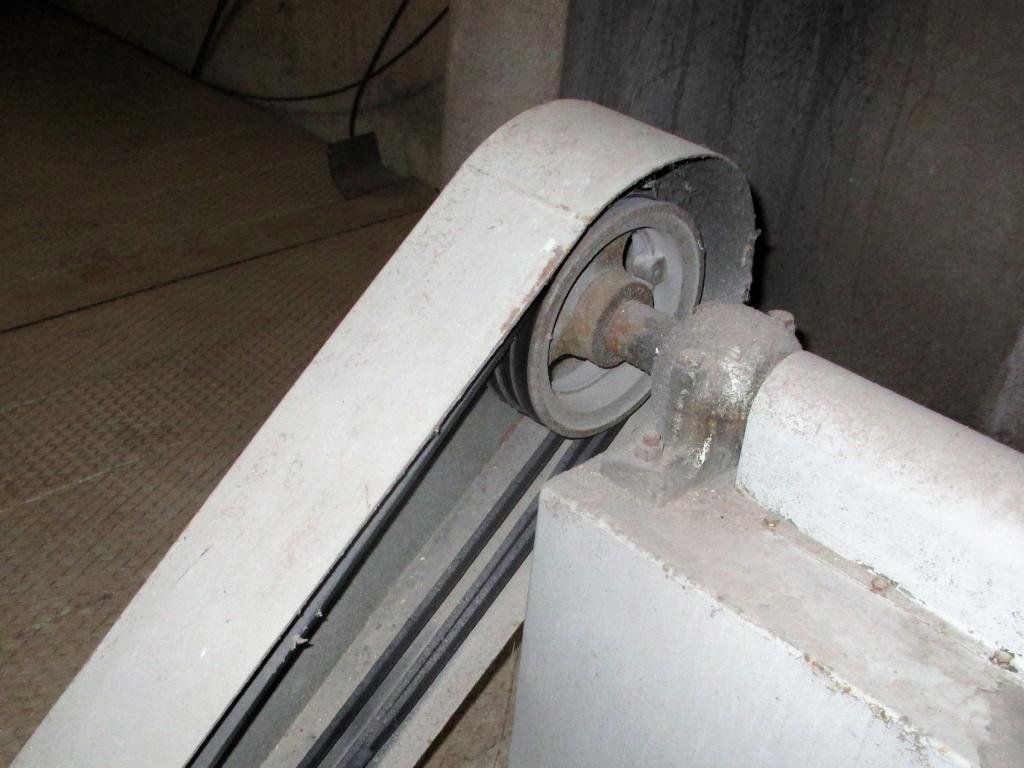 Ein altes Flaschenzugsystem mit abgenutztem Riemen und Betonstützen in einer düsteren Umgebung.