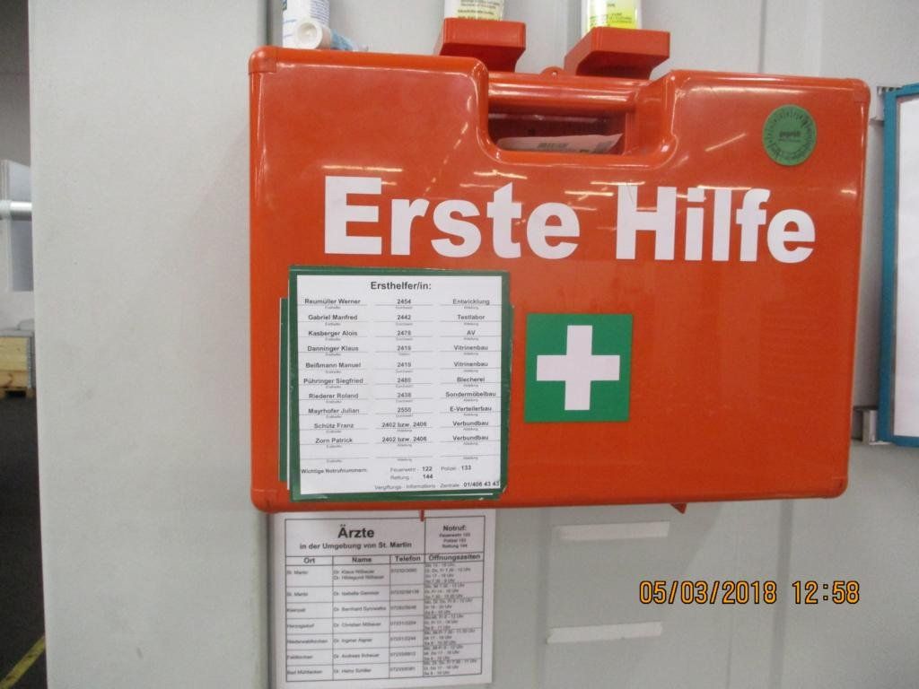 Orangefarbener Erste-Hilfe-Kasten mit grünem Kreuz und Inventarliste.