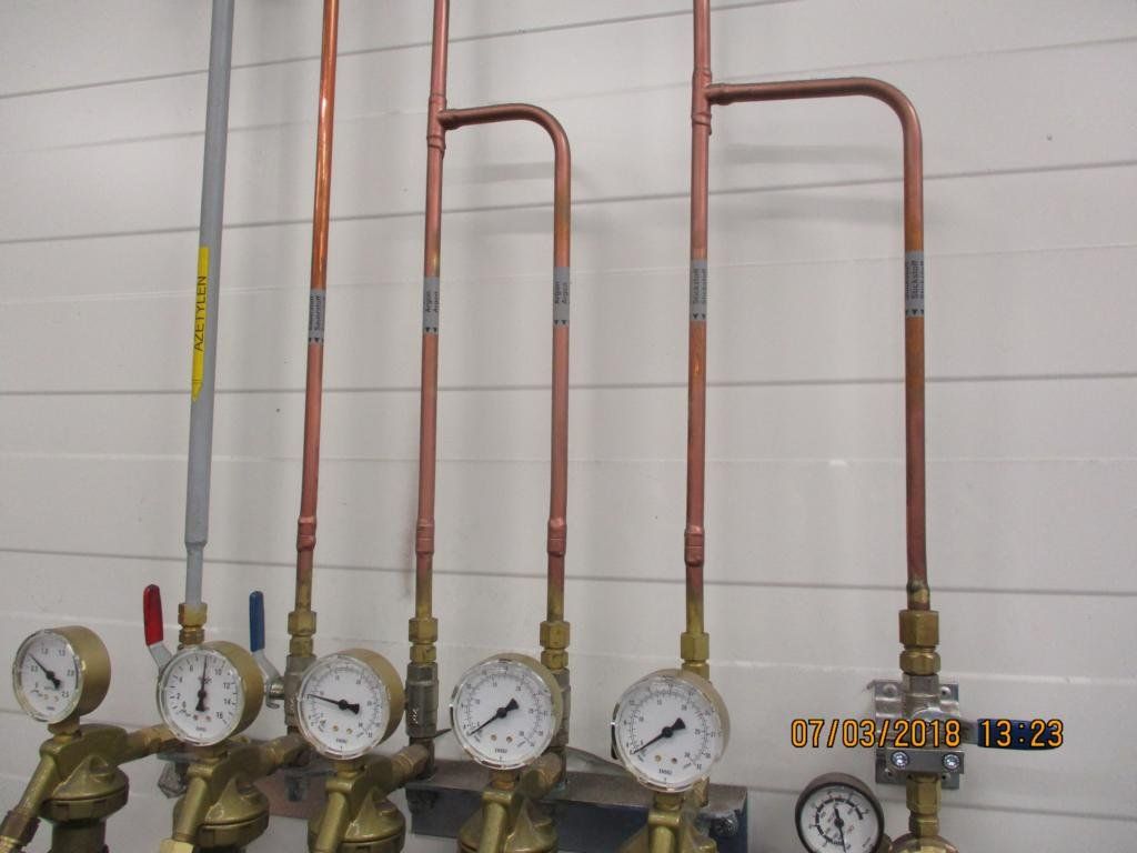 Kupferrohre mit Manometern und Ventilen, die an einer Wand montiert sind.