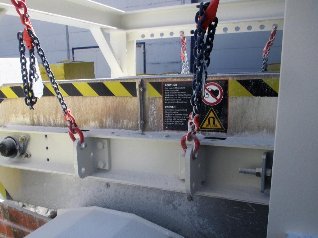 Nahaufnahme einer weißen Industriemaschine mit Sicherheitsketten und Warnhinweisen, die mit Staub bedeckt ist.