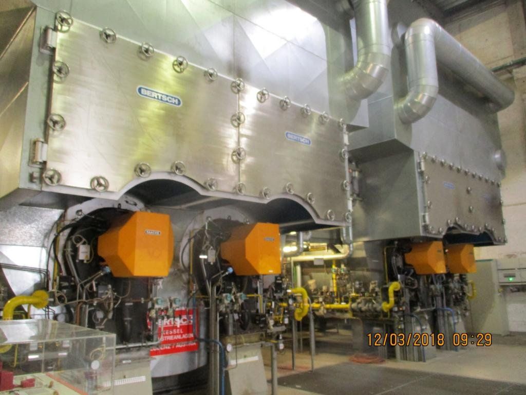 Großer Industrieofen mit orangefarbenen Brennern, silbernen Paneelen und gelben Rohren.