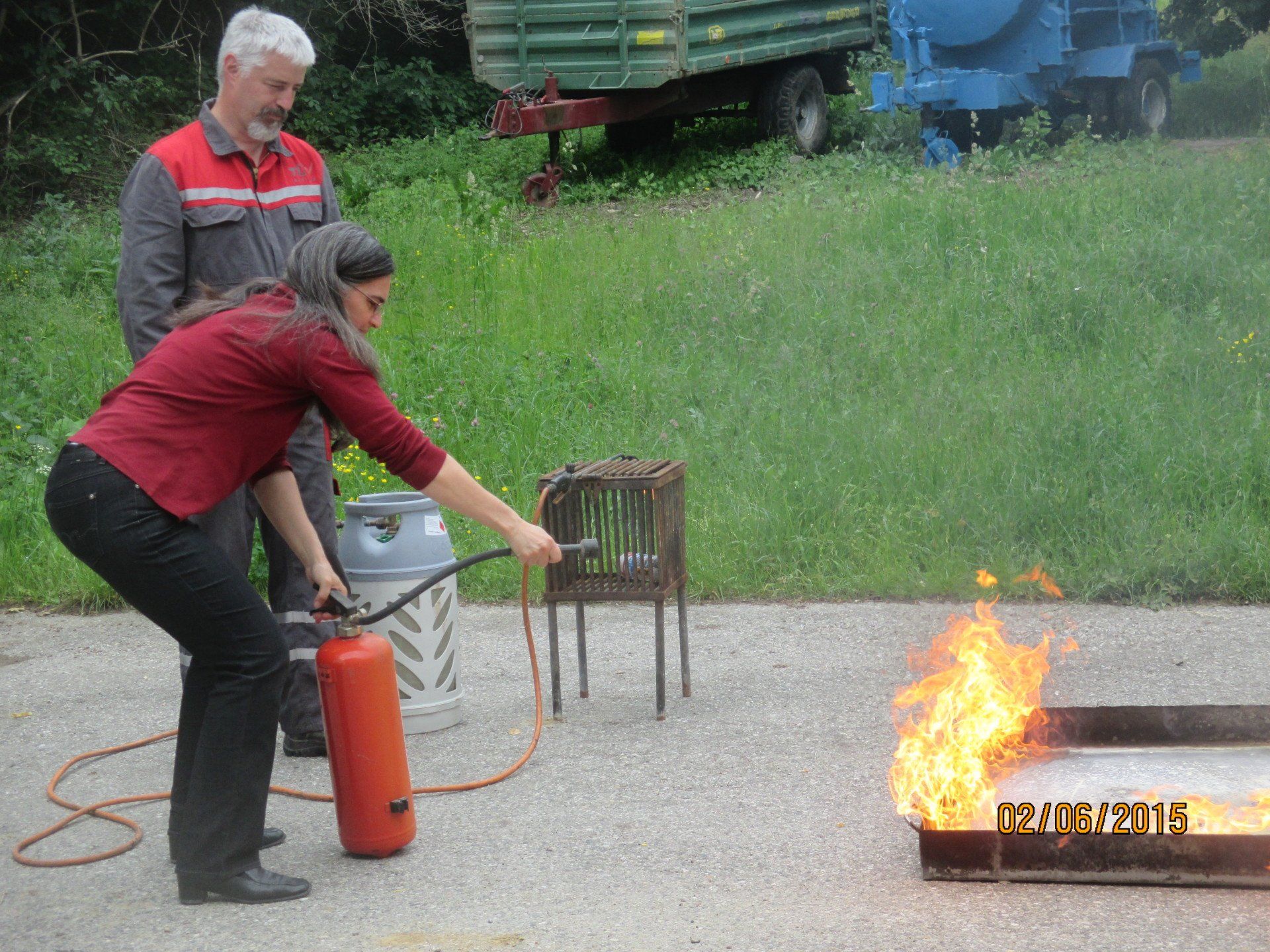 Eine Frau löscht einen kleinen Brand mit einem Feuerlöscher; ein Mann beobachtet sie von draußen.
