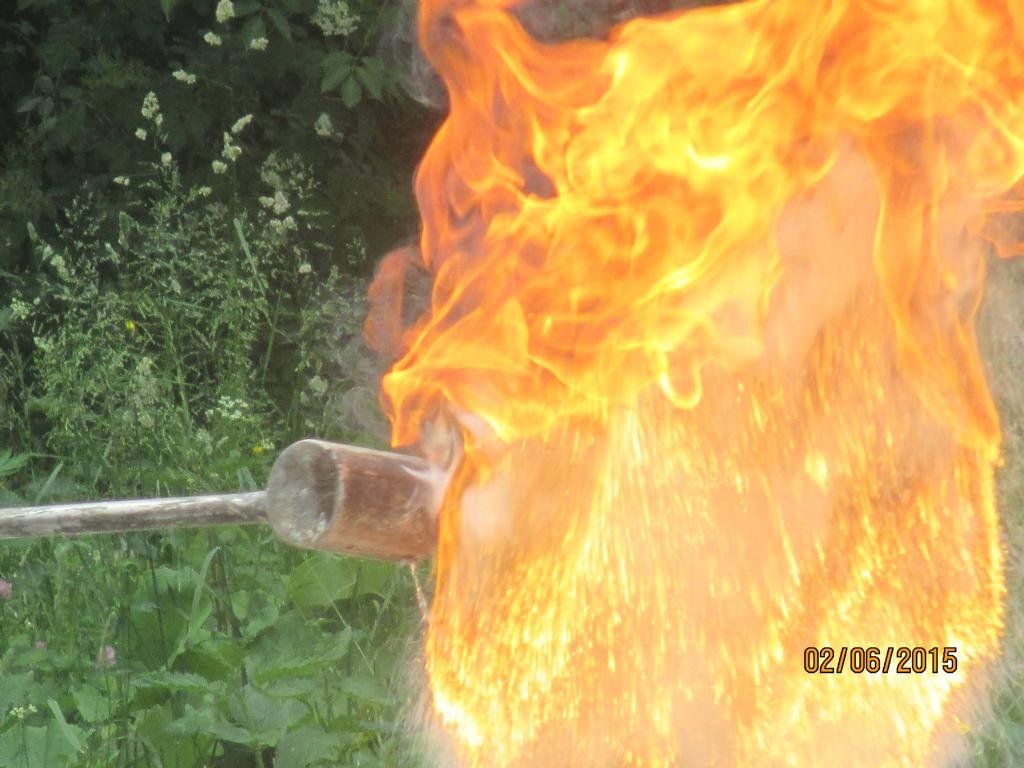 Aus einem Metallgerät schießt in der Nähe von Grünflächen im Freien eine große Flamme hervor.